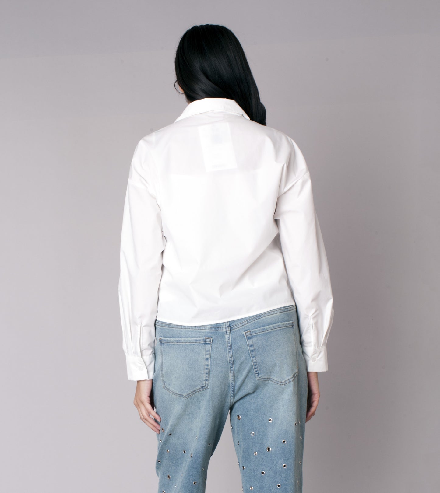White cropped button-down shirt with denim star patch detailing on the front, model showing back view styled with denim jeans For Her NYC