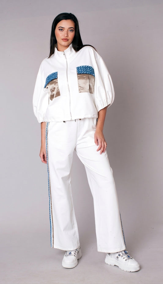 Woman wearing a white embellished track pant set with zip-front jacket, puff sleeves, satin pocket accents, and wide leg pants – For Her NYC