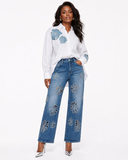 Model wearing a white button-down shirt with blue floral embroidery, paired with blue embellished jeans by For Her NYC