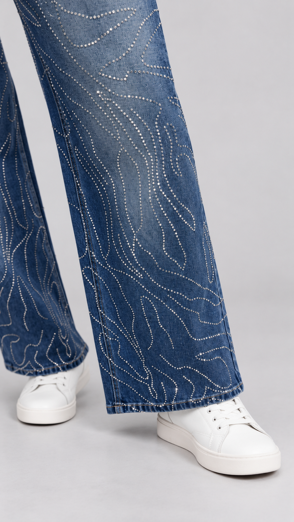 Hem close-up of a model wearing the For Her NYC Rhinestone Swirl Wide-Leg Denim Jeans - 83071 with curved rhinestone detailing