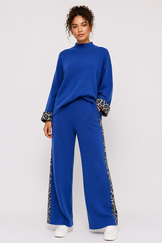 Model wearing the Leopard Trim Knit Lounge Set in royal blue featuring a relaxed mock neck top, wide-leg pants, and leopard trim accents on the cuffs and pant sides. For Her NYC.