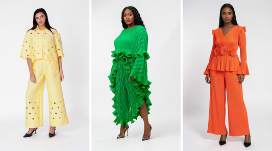 Three models in studio wearing bold statement outfits: yellow two-piece set with polka dot detail, emerald green ruffle-trim dress, and bright orange pleated two-piece set with floral waist accents – For Her NYC