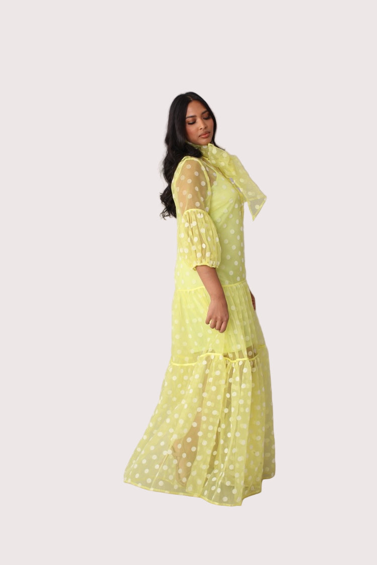 Polka dot organza maxi dress style 82234 in yellow and white shown in a side standing pose emphasizing the tiered skirt and elegant length by For Her NYC