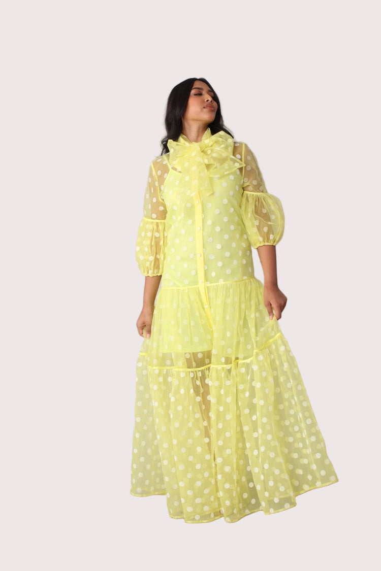 Polka dot organza maxi dress style 82234 in yellow and white shown in a side standing pose emphasizing the tiered skirt and elegant length by For Her NYC
