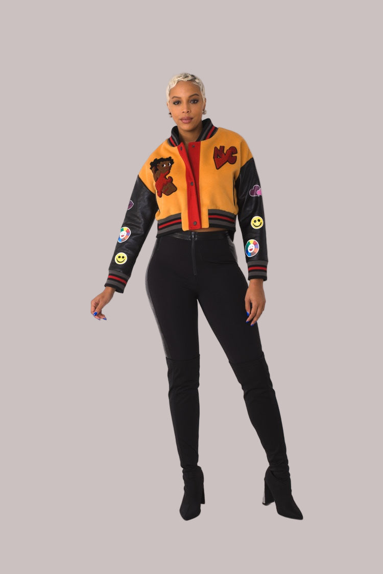 Betty Boop varsity crop jacket style 82236 in orange and black shown front-facing in a standing pose highlighting the bold color contrast and cropped silhouette by For Her NYC