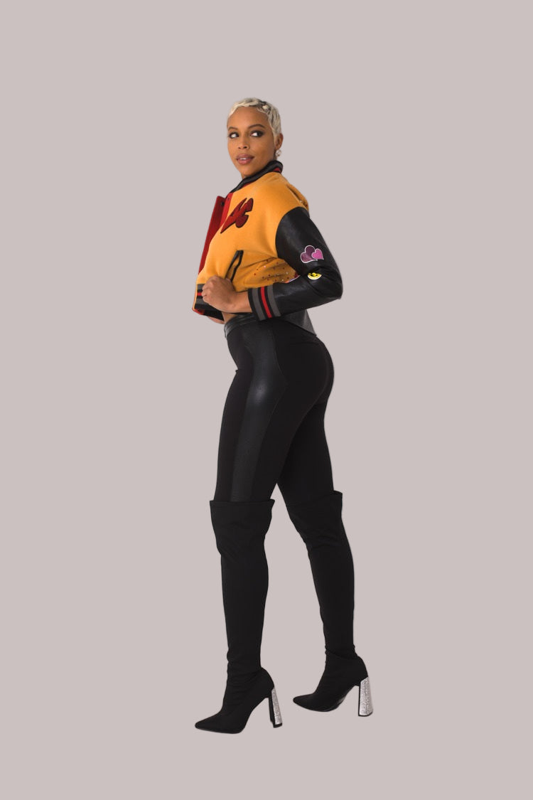 Betty Boop varsity crop jacket style 82236 in orange and black shown in a three-quarter standing pose highlighting varsity details and character patches by For Her NYC