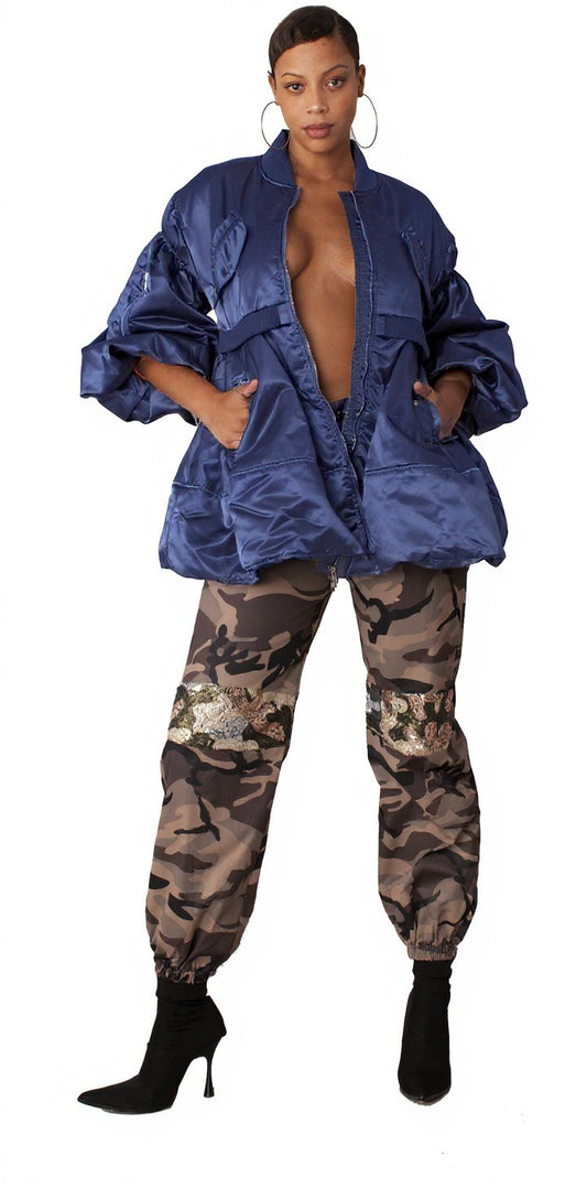 Model wearing navy and silver woven jacket with contrasting lining paired with camo pants and black ankle boots, standing front pose – For Her NYC