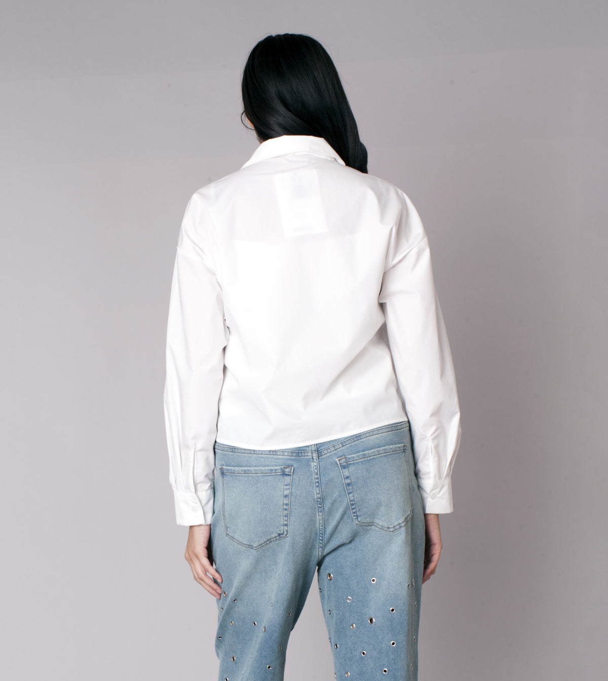 White cropped button-down shirt with denim star patch detailing on the front, model showing back view styled with denim jeans For Her NYC