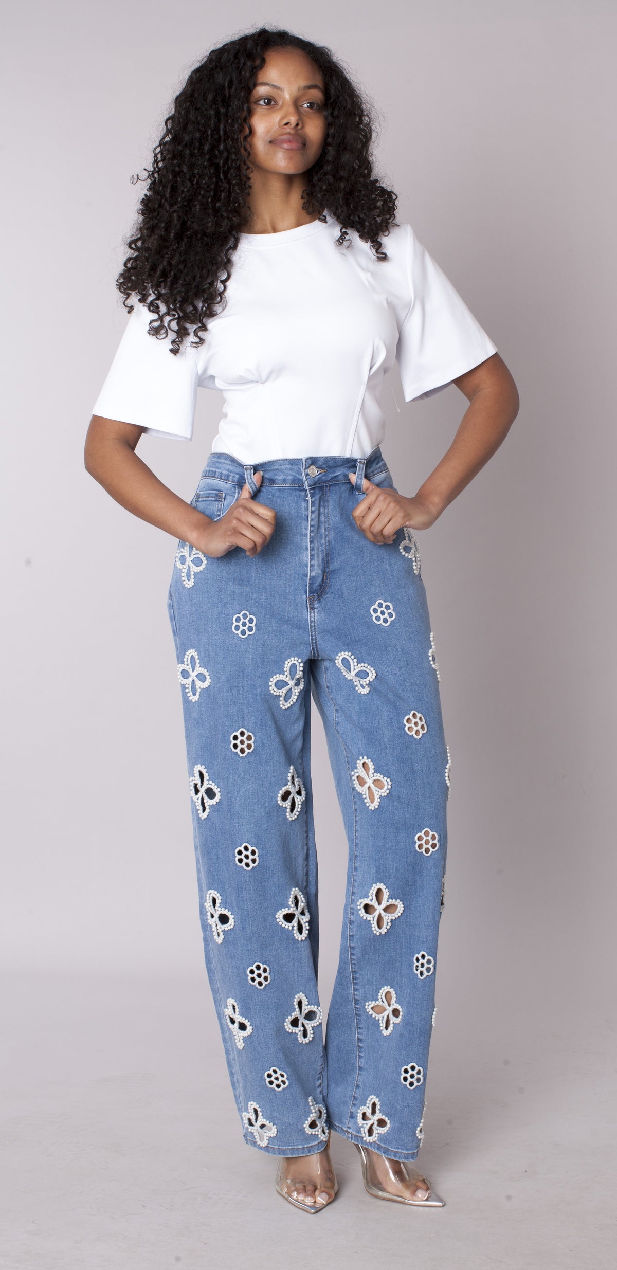 Blue denim wide-leg jeans featuring floral cutout embellishments throughout, model standing full length front view styled with white top For Her NYC