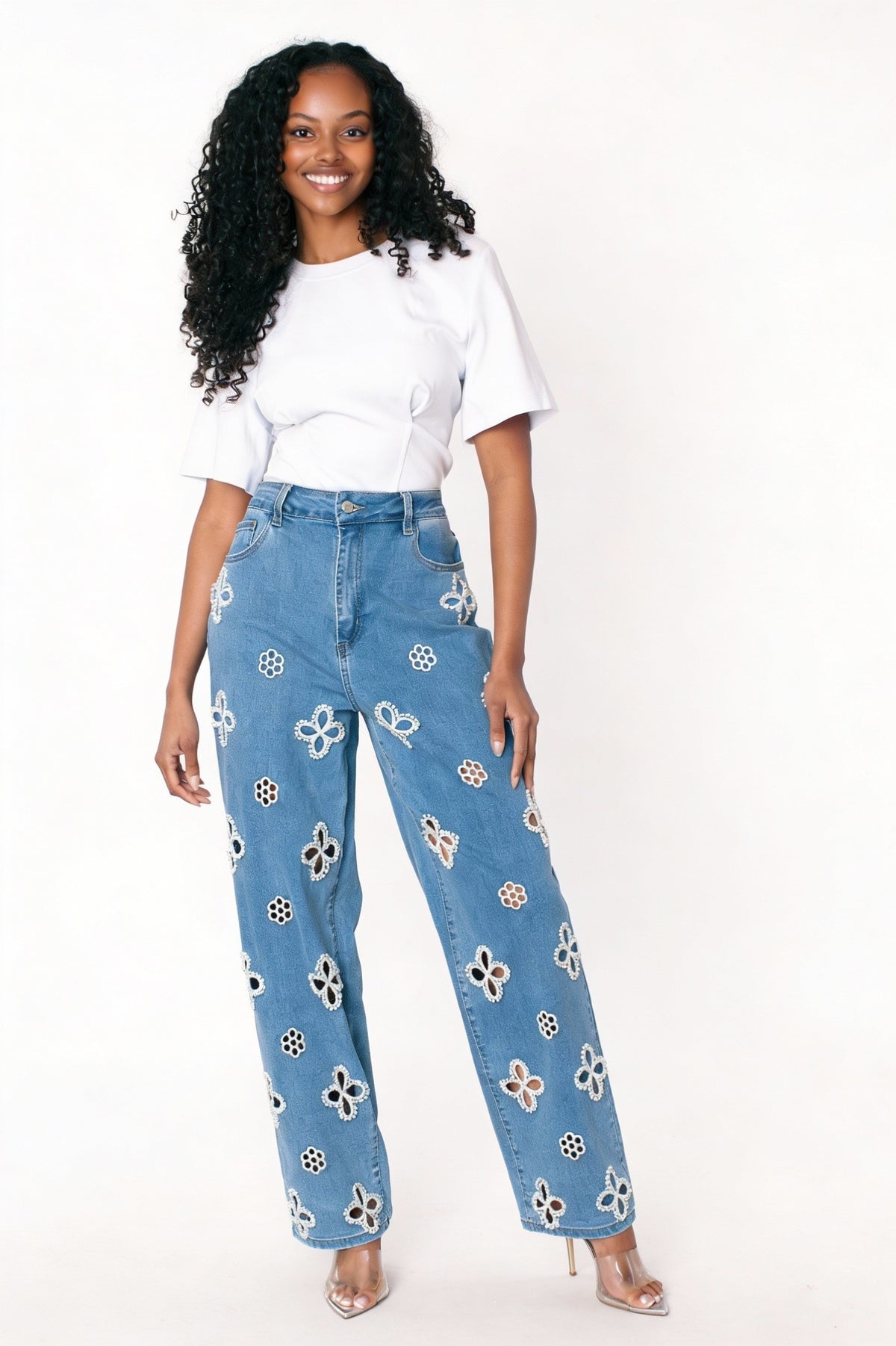 Denim wide-leg jeans with intricate floral cutout embellishments, model standing facing forward with one hand on hip wearing white top For Her NYC