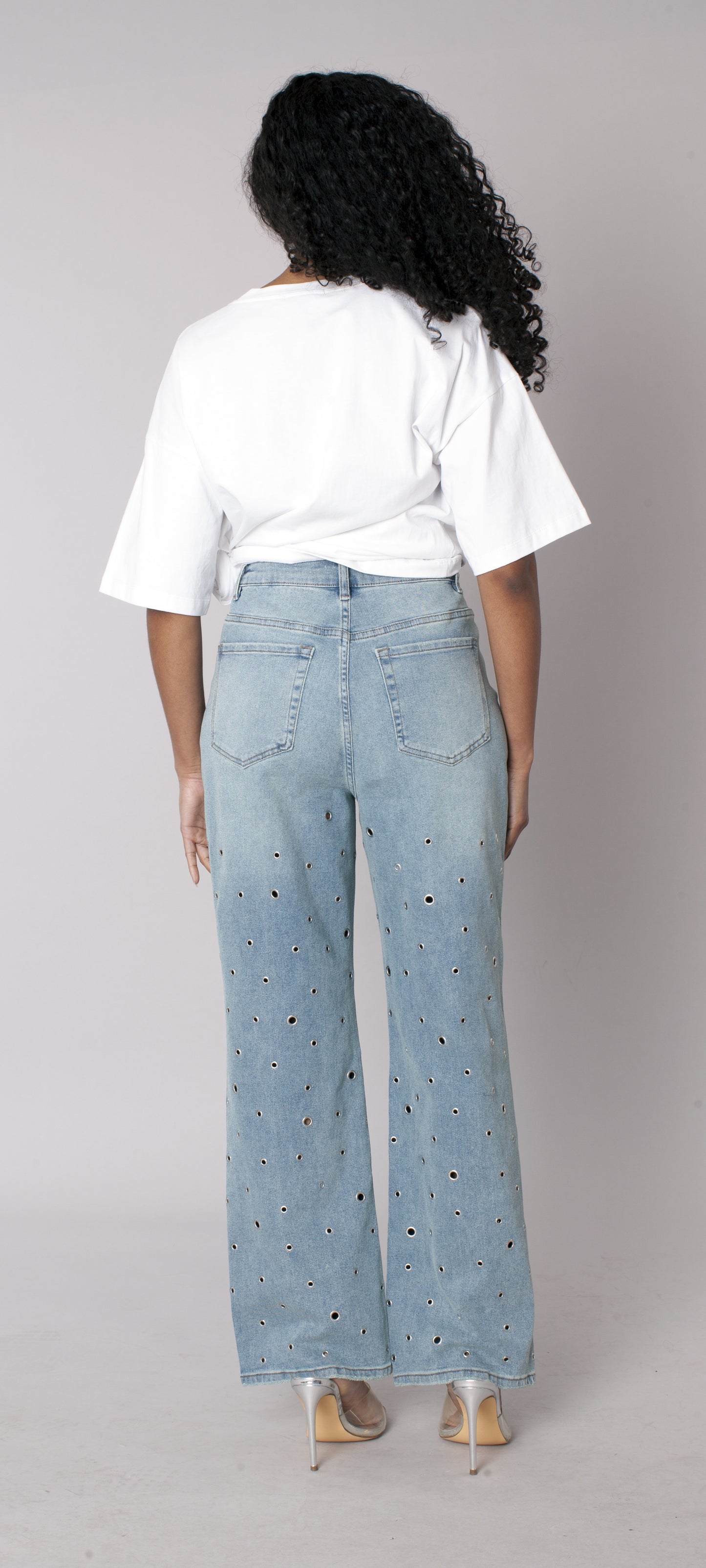 Medium wash straight-leg denim jeans featuring grommet detailing, model showing back view styled with graphic tee For Her NYC