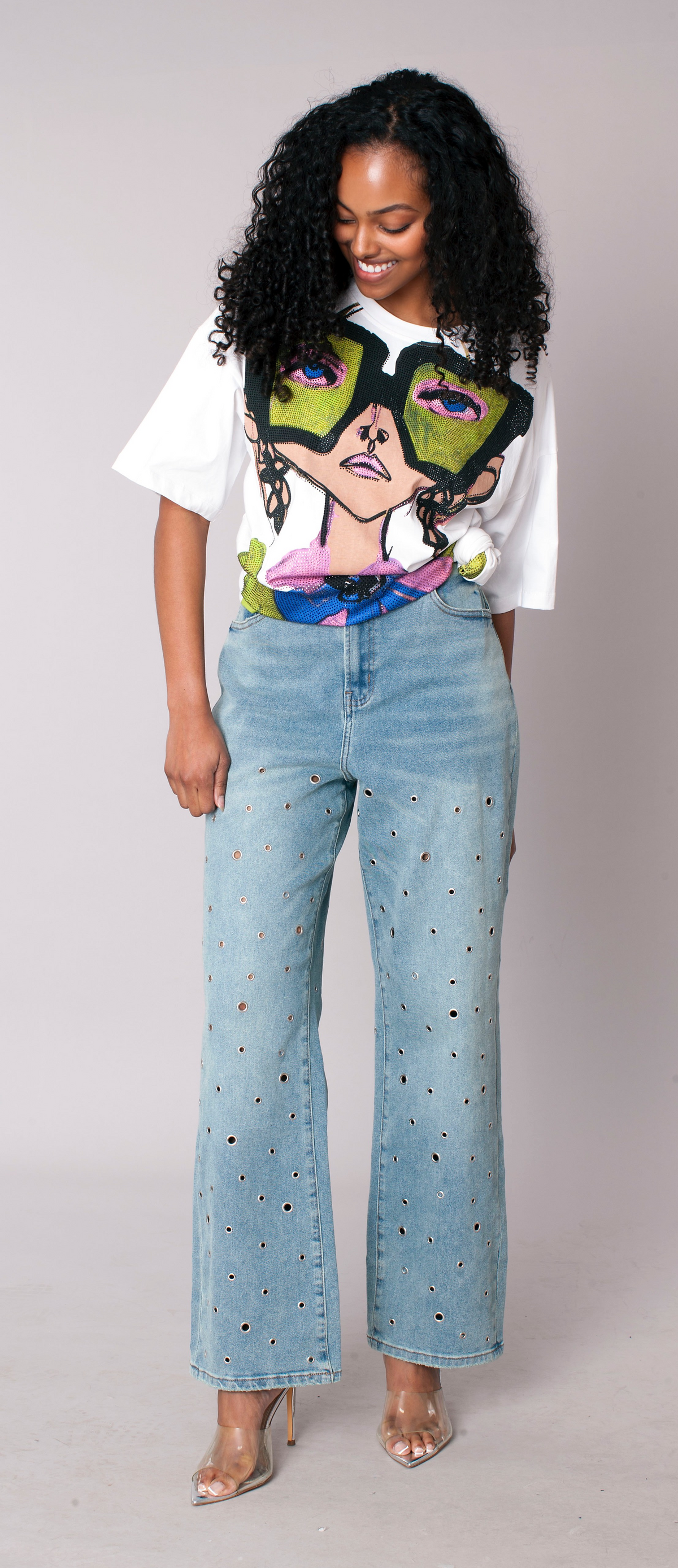 Medium wash straight-leg denim jeans with grommet embellishment details, model standing facing forward looking down wearing graphic tee For Her NYC