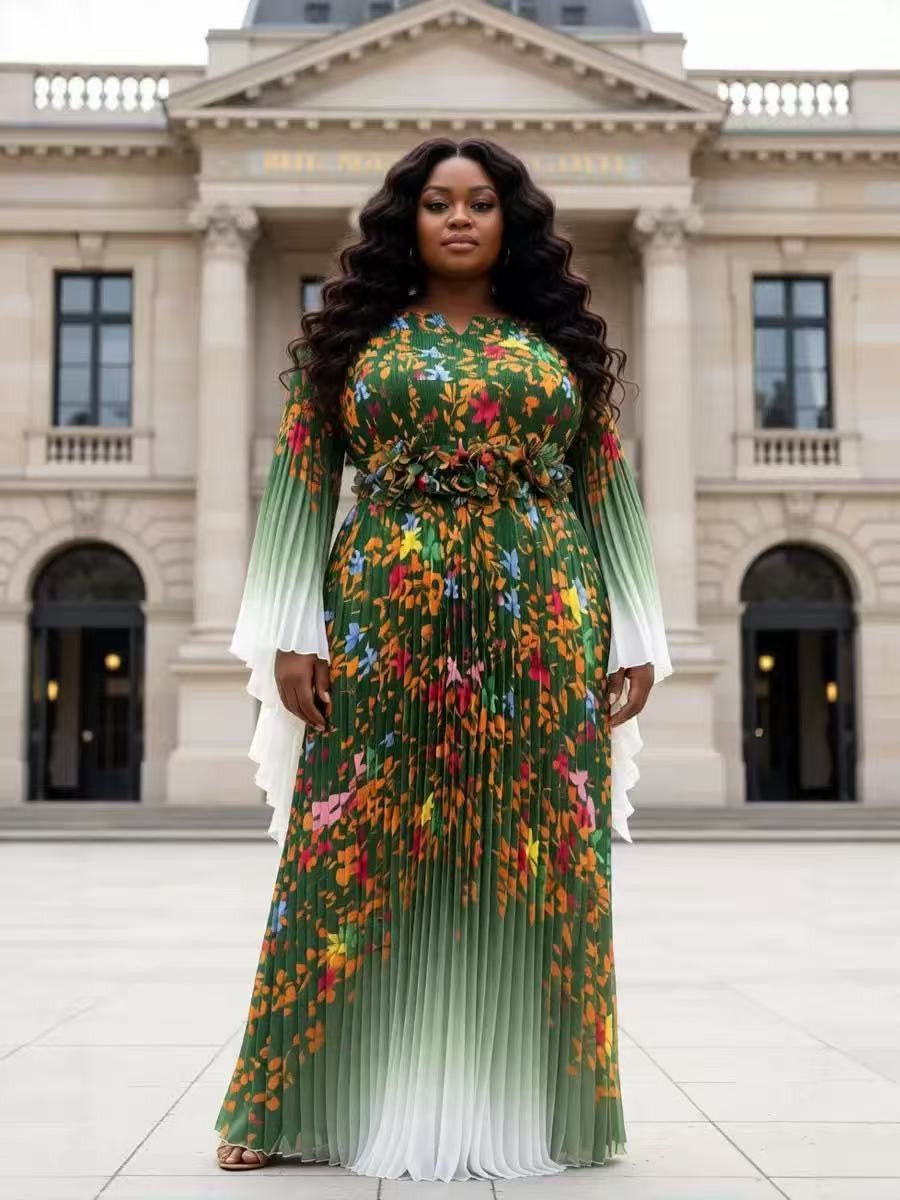 Emerald green floral pleated maxi dress with sheer long sleeves and statement waist detail modeled in a front-facing pose outdoors For Her NYC