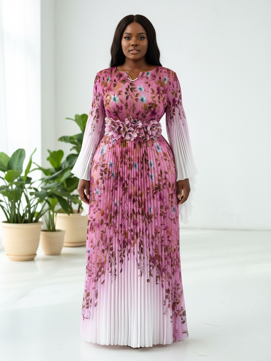 Pink multi floral pleated maxi dress with statement waist detail and sheer long sleeves modeled in a front-facing pose against a bright studio background For Her NYC