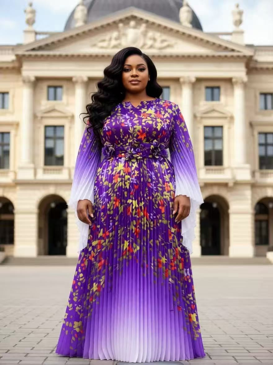 Purple floral pleated maxi dress with statement waist detail and sheer sleeves modeled outdoors in front of elegant city architecture For Her NYC