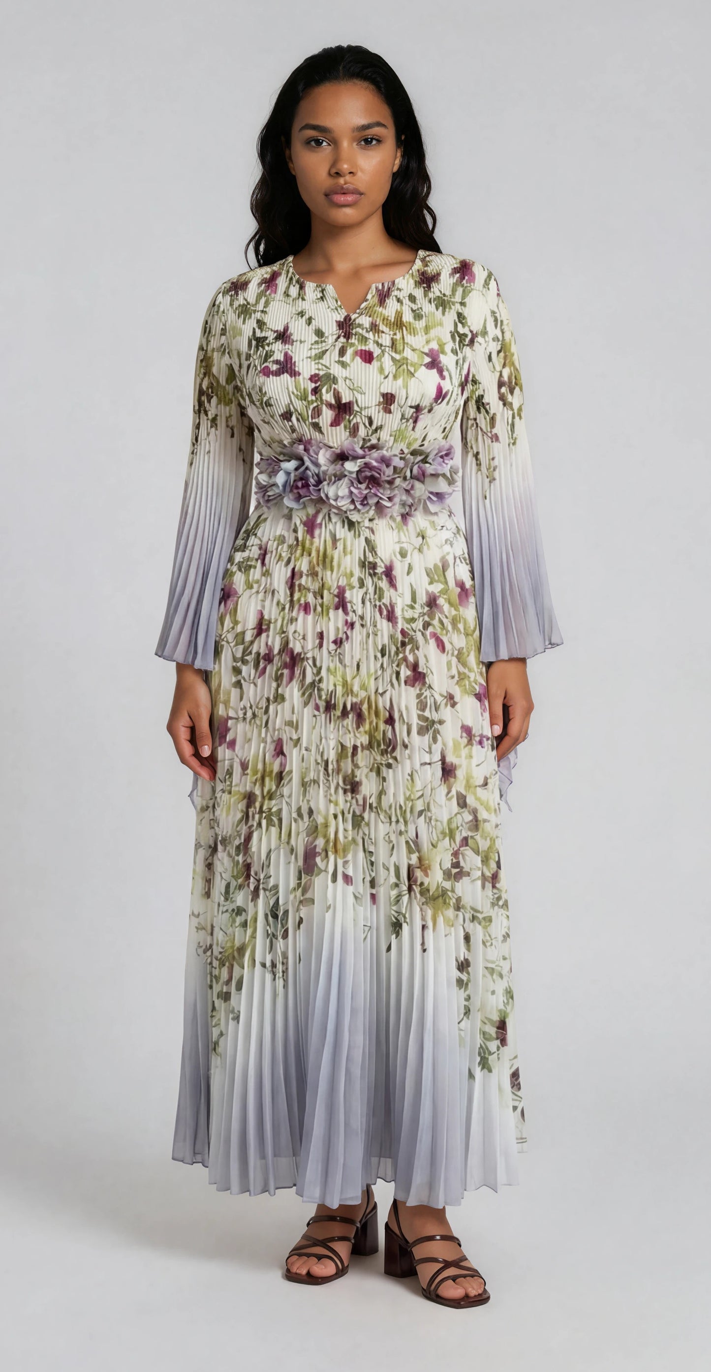 Silver multi floral pleated maxi dress with flowing pleats and sheer sleeves modeled in a clean studio setting For Her NYC