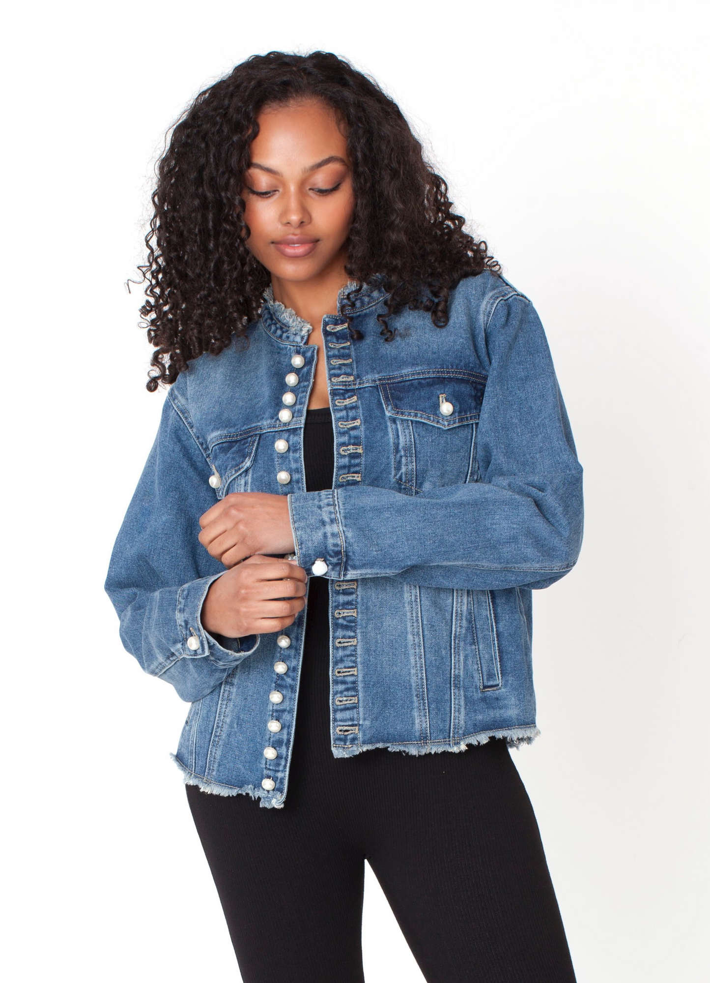 Denim jacket featuring pearl button detailing and classic structured silhouette, model holding lapels styled with black top and pants For Her NYC