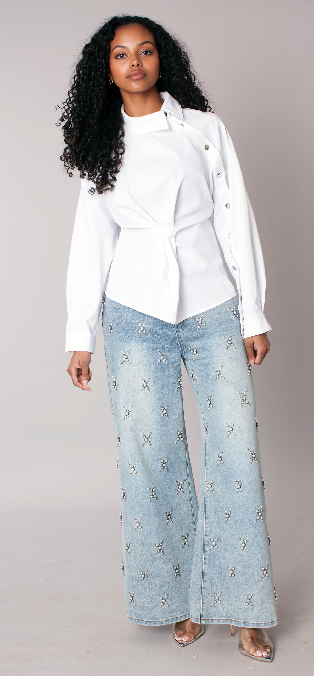 Light wash wide-leg denim jeans with starburst pearl embellishments throughout, model standing front view styled with white top For Her NYC