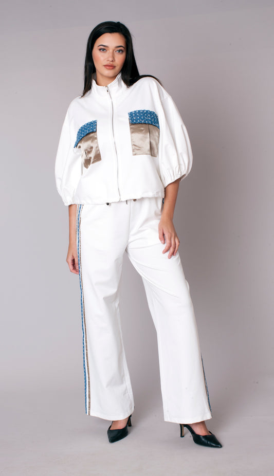 Woman wearing a white embellished track pant set with zip-front jacket, puff sleeves, satin pocket accents, and wide leg pants – For Her NYC