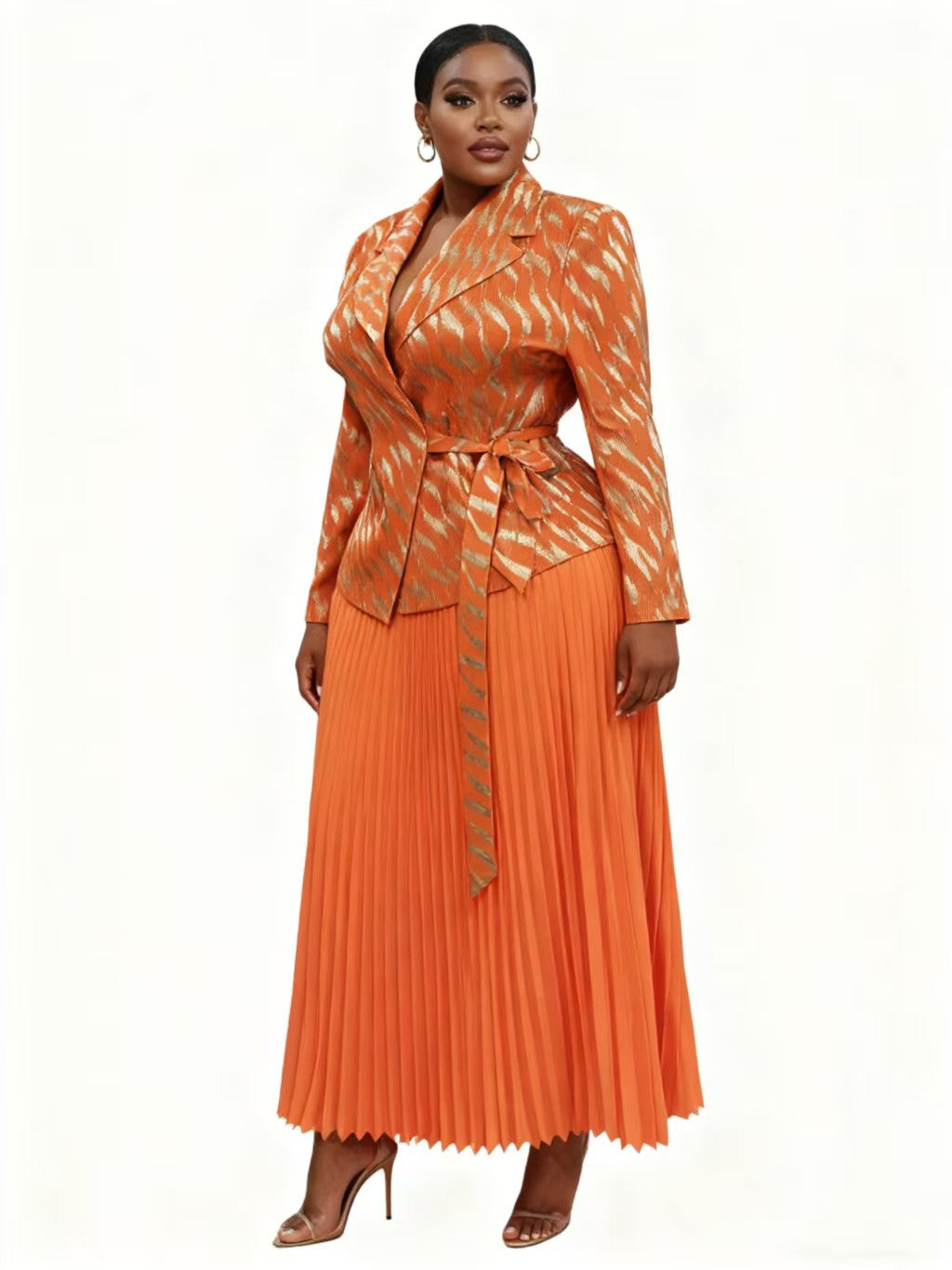 Woman wearing a flowing orange pleated midi skirt with a coordinating patterned wrap-style jacket and tie waist, styled with heels — For Her NYC