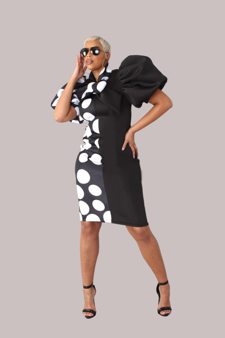 Model wearing black and white dot puff sleeve midi dress with bow tie collar, front-facing hero pose highlighting patterned fabric and tailored silhouette by For Her NYC