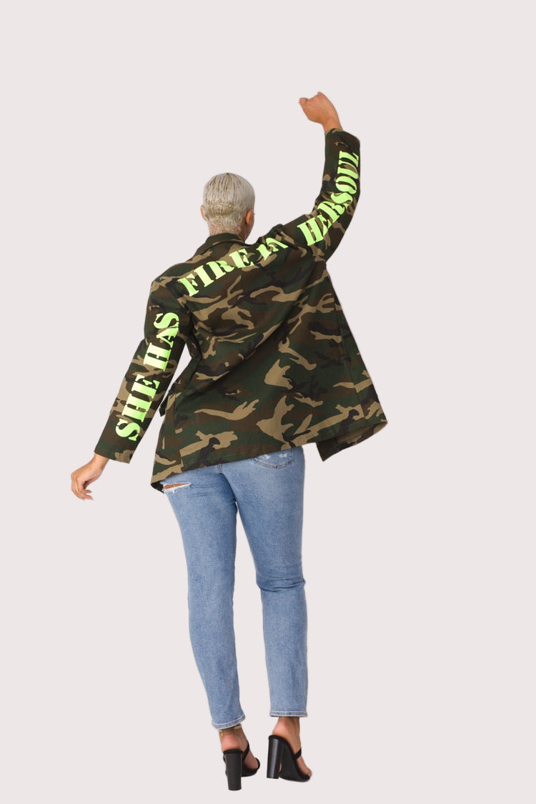 Model wearing camouflage utility jacket, dynamic pose with arm raised highlighting casual streetwear attitude and bold camo pattern by For Her NYC