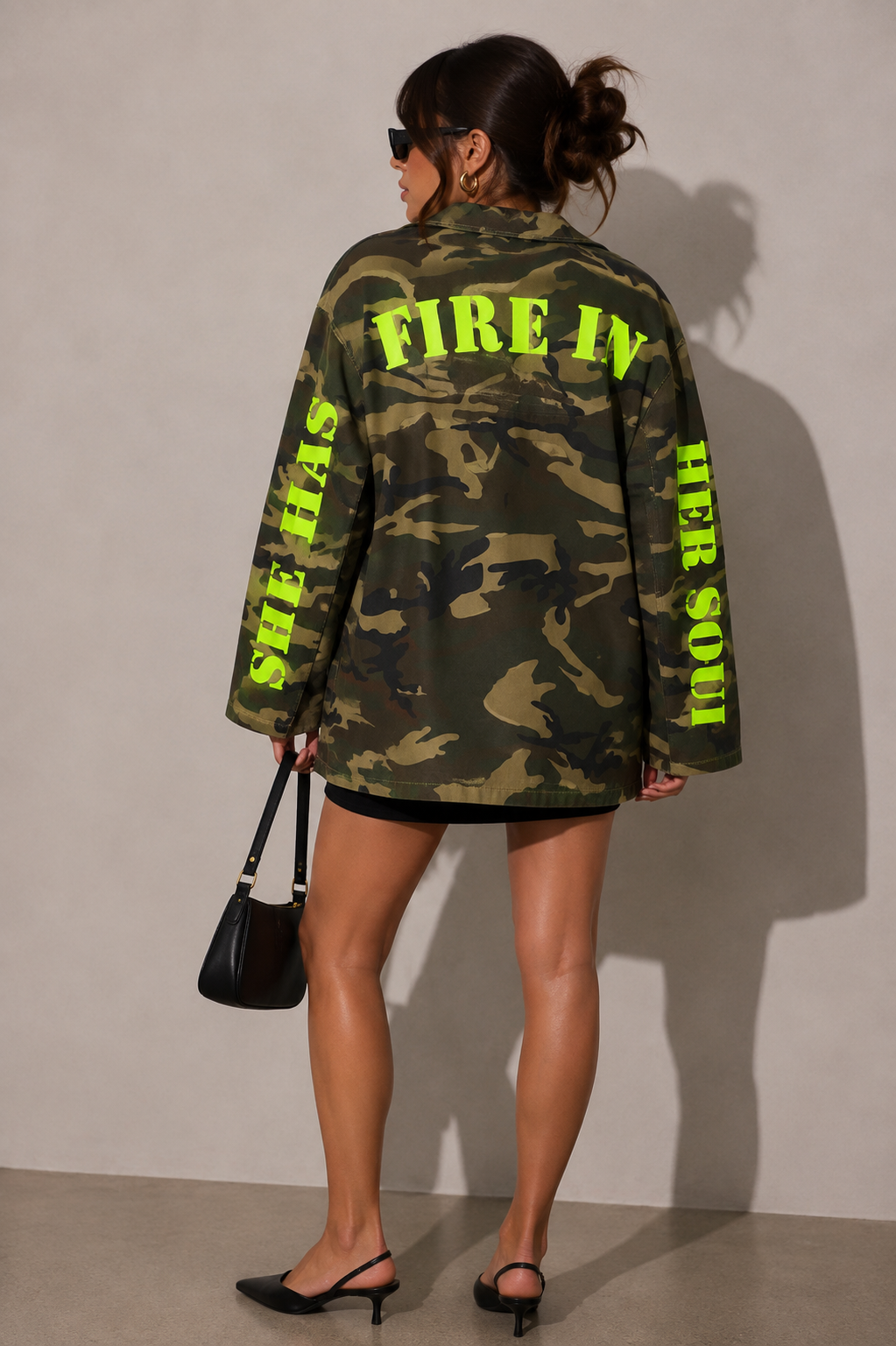 Model wearing camouflage utility jacket, dynamic pose with arm raised highlighting casual streetwear attitude and bold camo pattern by For Her NYC