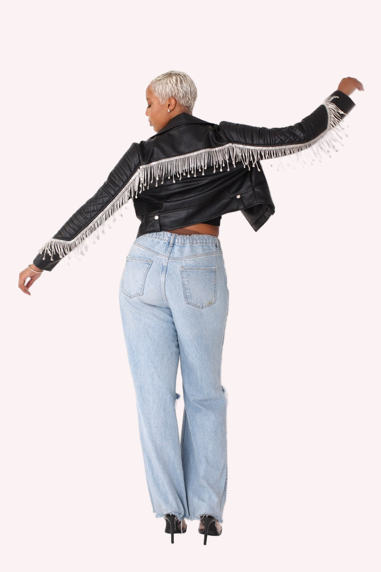 Full back view of a black cropped faux leather jacket with arms extended, highlighting the draped fringe detailing across the back, quilted sleeves, cropped length, and statement movement of the design by For Her NYC