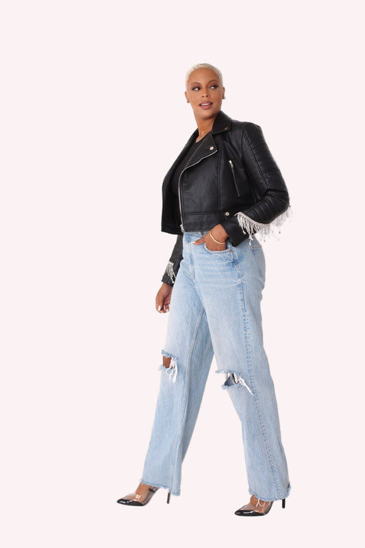 Model wearing a black cropped faux leather jacket with fringe cuff detailing shown from the front, highlighting the quilted sleeves, zip-up front, and cropped silhouette styled with light denim by For Her NYC