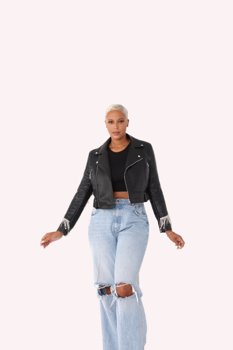 Model wearing a black cropped faux leather jacket in a relaxed front standing pose, highlighting the zip-front closure, quilted sleeves, and statement fringe accents by For Her NYC