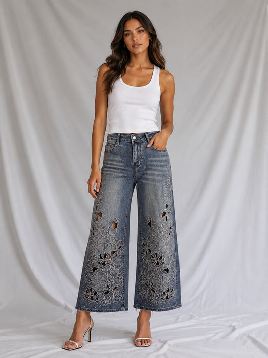 Model wearing the Crystal Floral Embellished Wide-Leg Jeans in blue denim featuring shimmering crystal floral embellishments, a high-rise waist, and a relaxed wide-leg silhouette paired with a white tank top. For Her NYC.