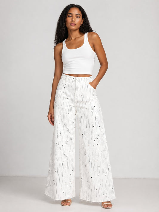 Model wearing the Crystal Stardust Embellished White Denim Jeans in white denim featuring sparkling crystal embellishments, a high-rise waist, and a wide-leg silhouette paired with a white tank top. For Her NYC.