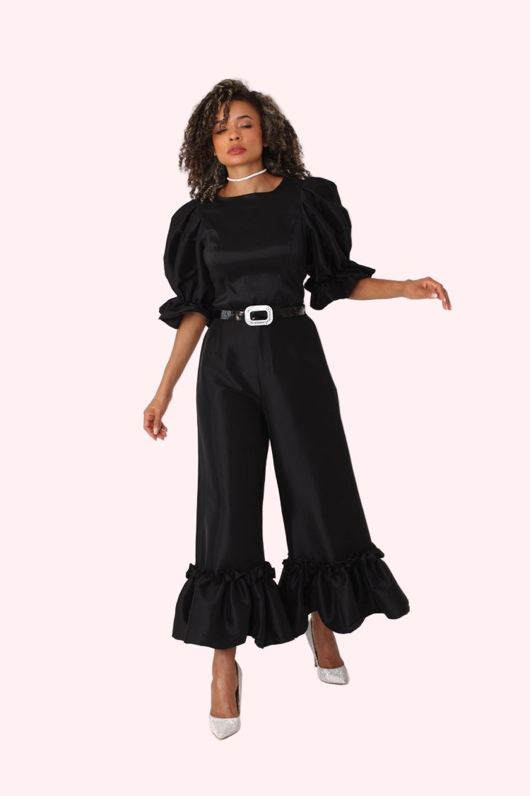 Model posing with arms crossed in black dramatic ruffle hem wide leg pants highlighting tailored waist by For Her NYC