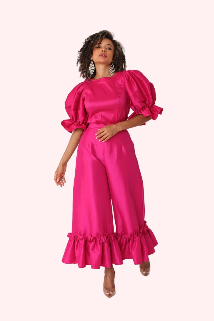 Model walking forward in fuchsia dramatic ruffle hem wide leg pants emphasizing flow and ruffle hem by For Her NYC