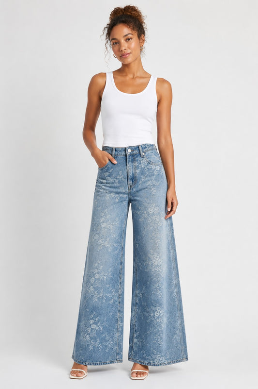 Model wearing the Floral Washed Wide-Leg Denim Pants in a light wash featuring a vintage-inspired floral wash, a high-rise waist, and a flattering wide-leg silhouette paired with a white tank top. For Her NYC.