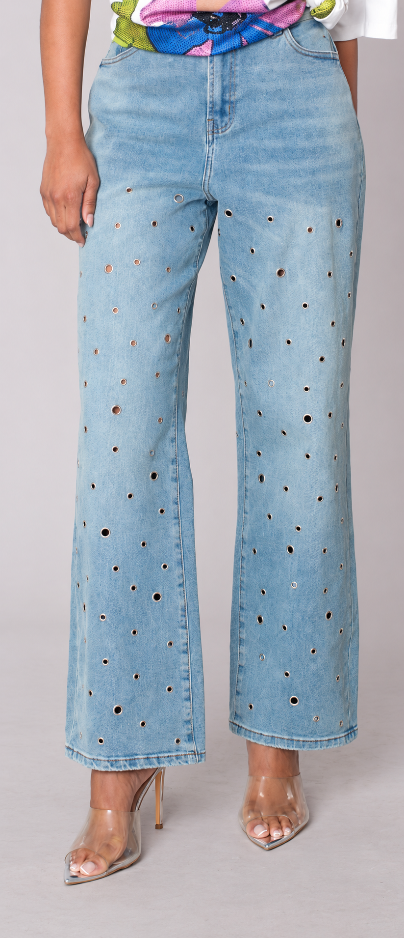 Front detail view of a model wearing the medium wash For Her NYC Grommet Detail Straight Leg Jeans - 82989 with mixed-size silver grommets throughout the legs