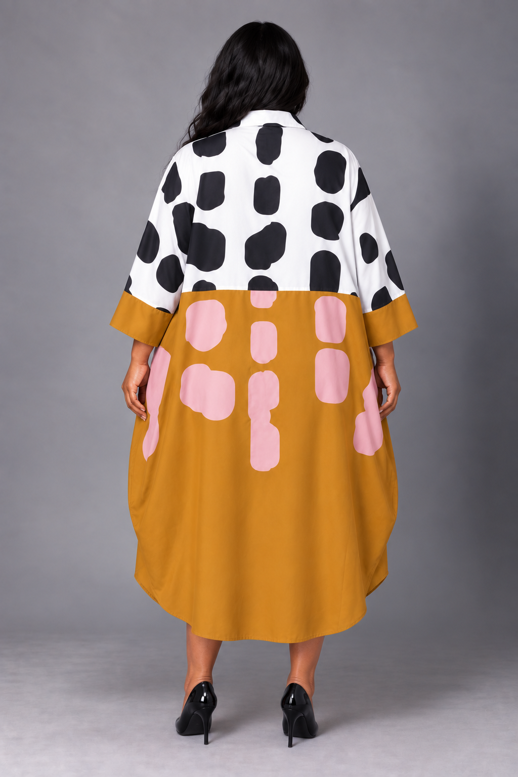 Back view of a plus-size model wearing the For Her NYC Plus Size Bold Graphics Shirt Dress - S0270W in mustard yellow, white, black, and pink with an abstract print and three-quarter sleeves
