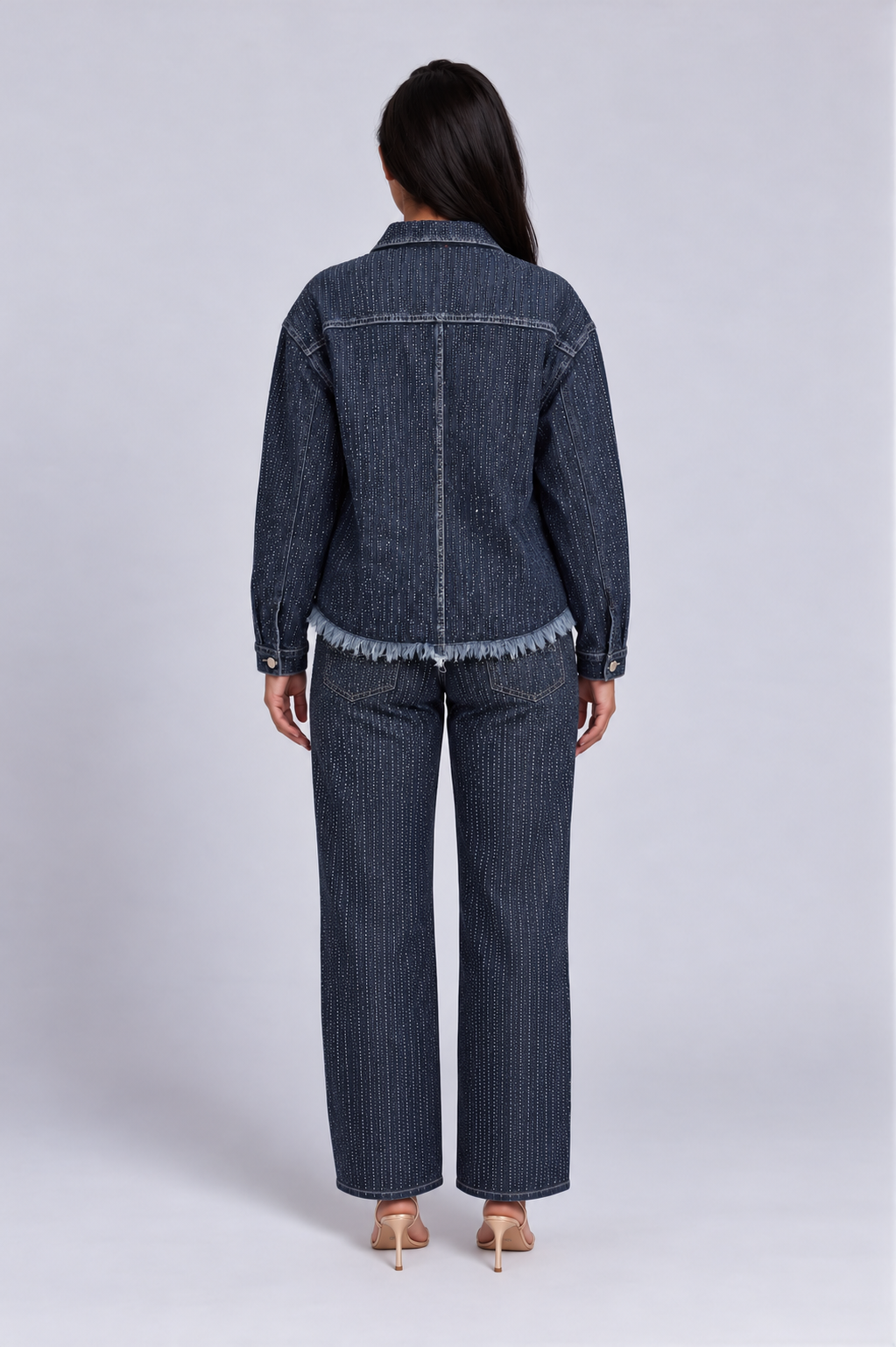 Back view of a model wearing the For Her NYC Rhinestone Embellished Denim Jacket - 82978 with vertical rhinestone rows and a frayed hem