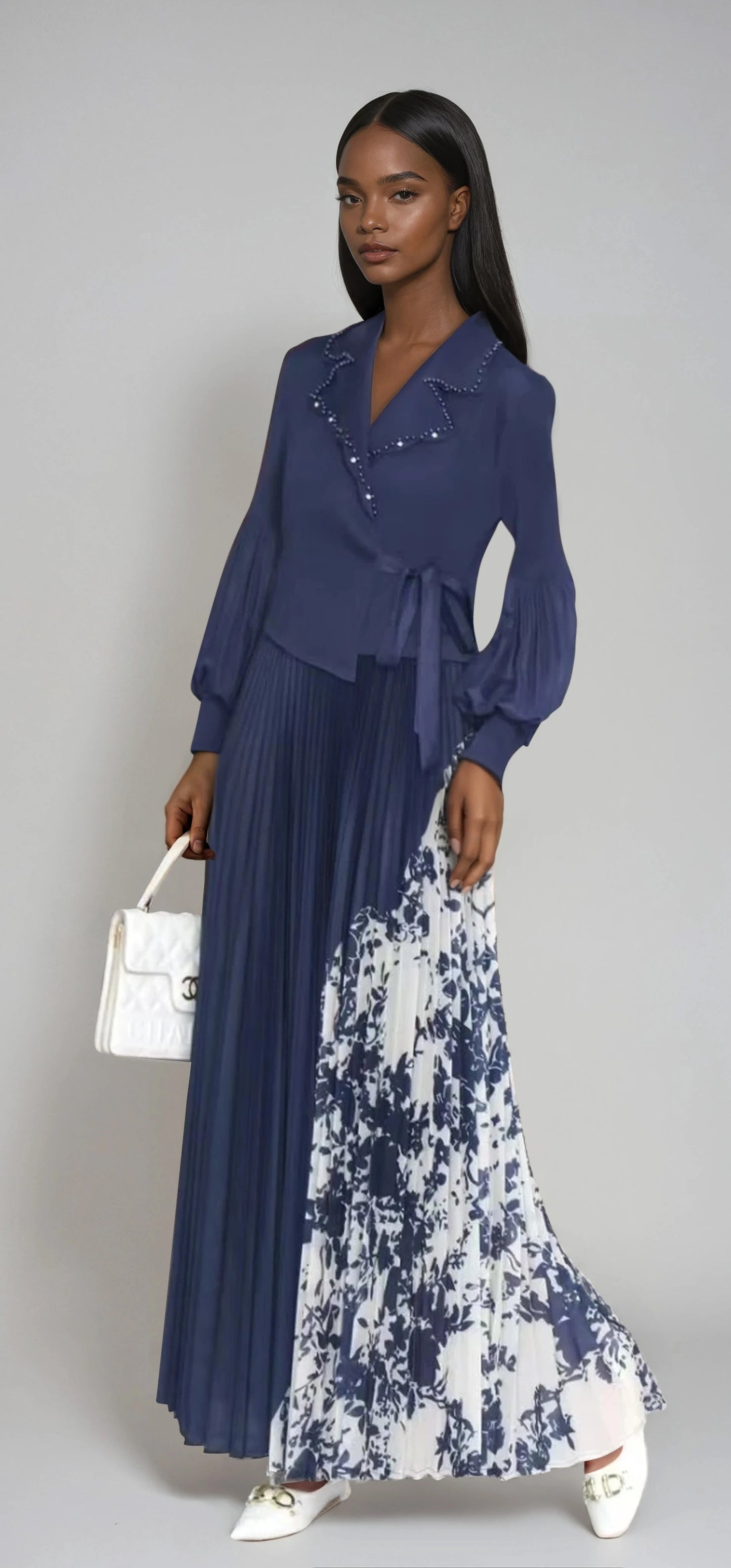 Model wearing navy pleated wrap dress with printed contrast skirt and belted waist by For Her NYC.