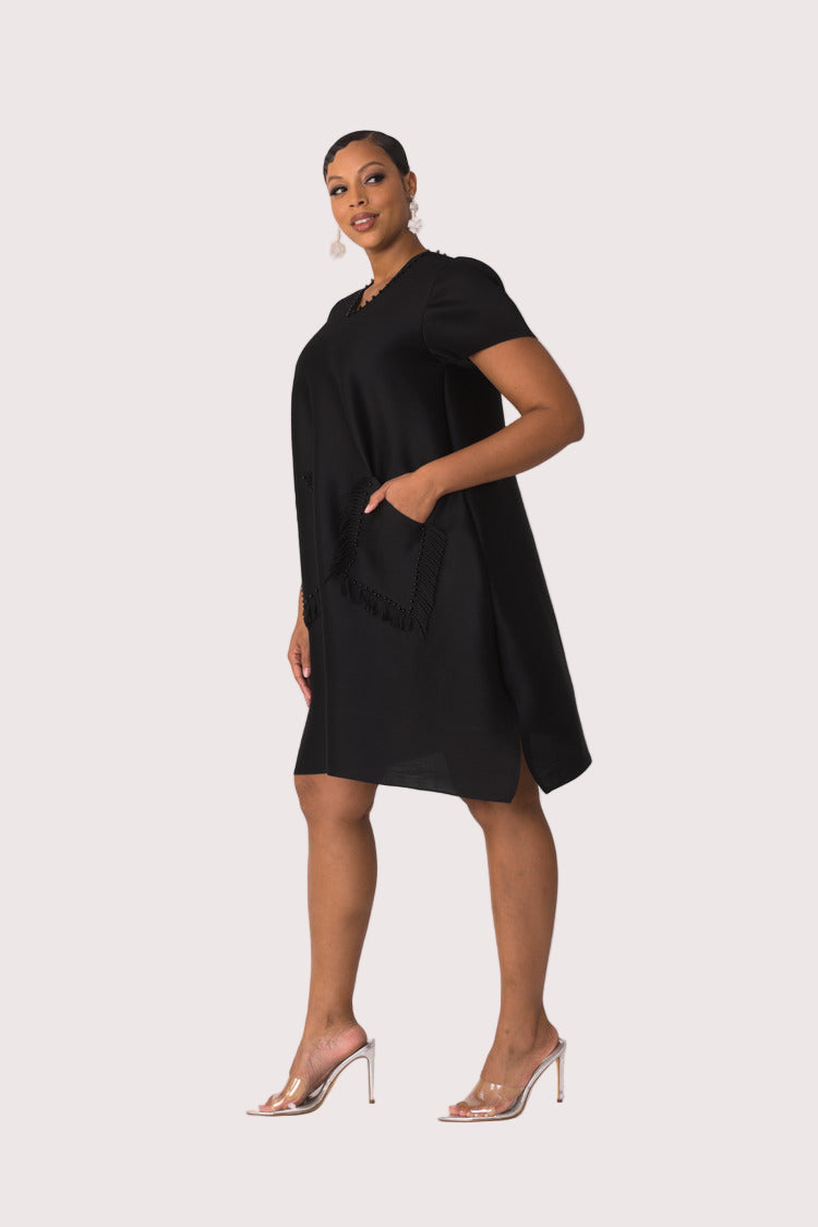 Three quarter angled view of model wearing the black fringe pocket shift dress highlighting fringe pocket detail and studded trim by For Her NYC