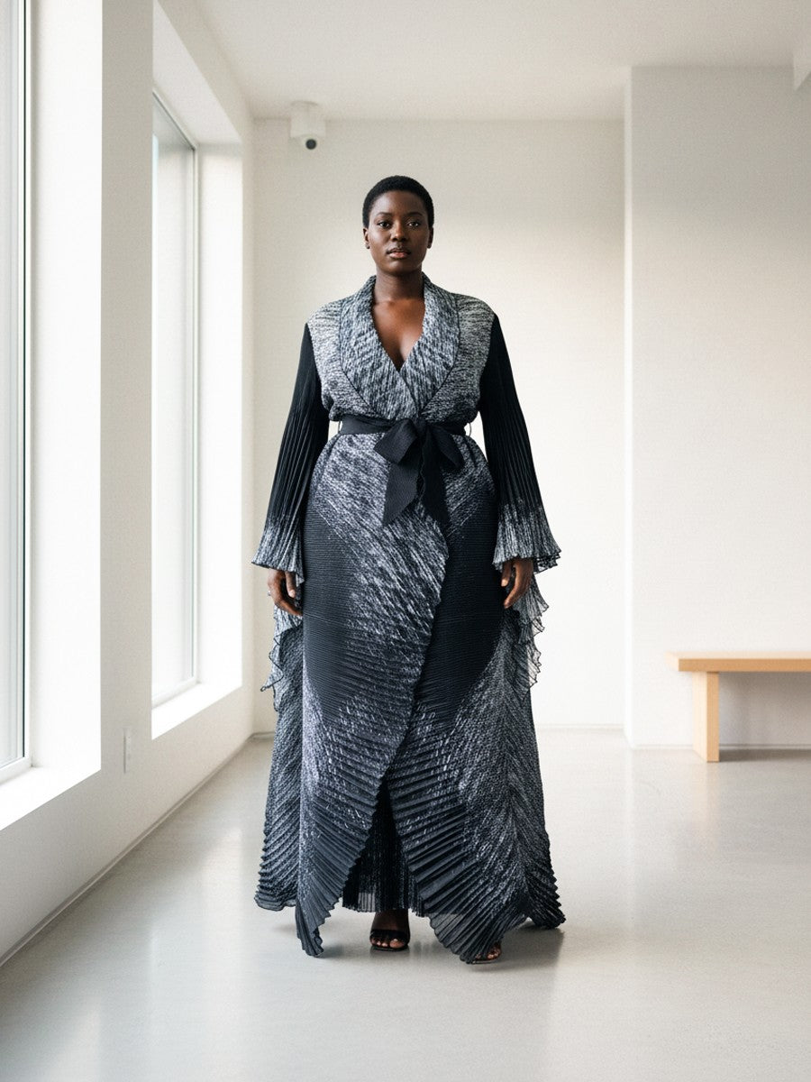 Full-length view of model wearing a black pleated wrap dress with wrap silhouette and flowing skirt, For Her NYC