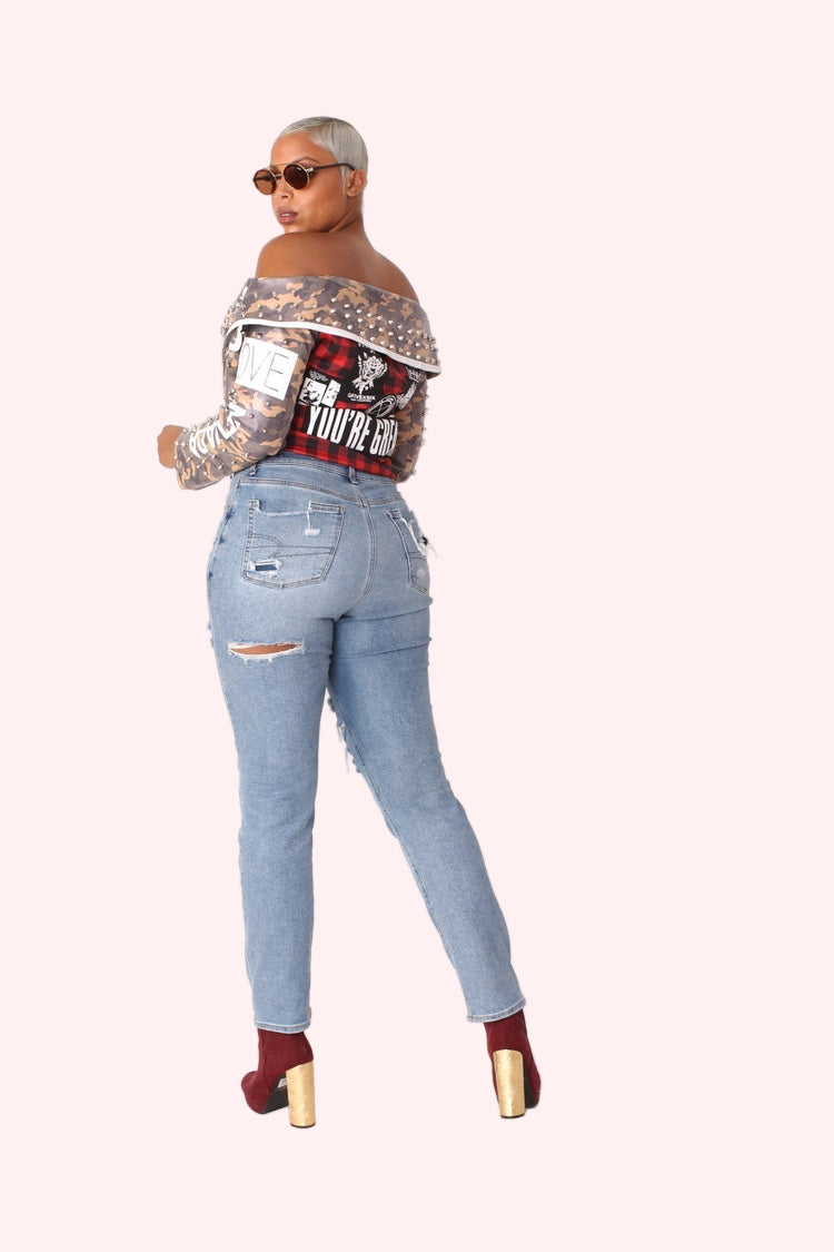 Back view pose of model wearing off-shoulder camo leather jacket featuring plaid panel and bold graphic patches