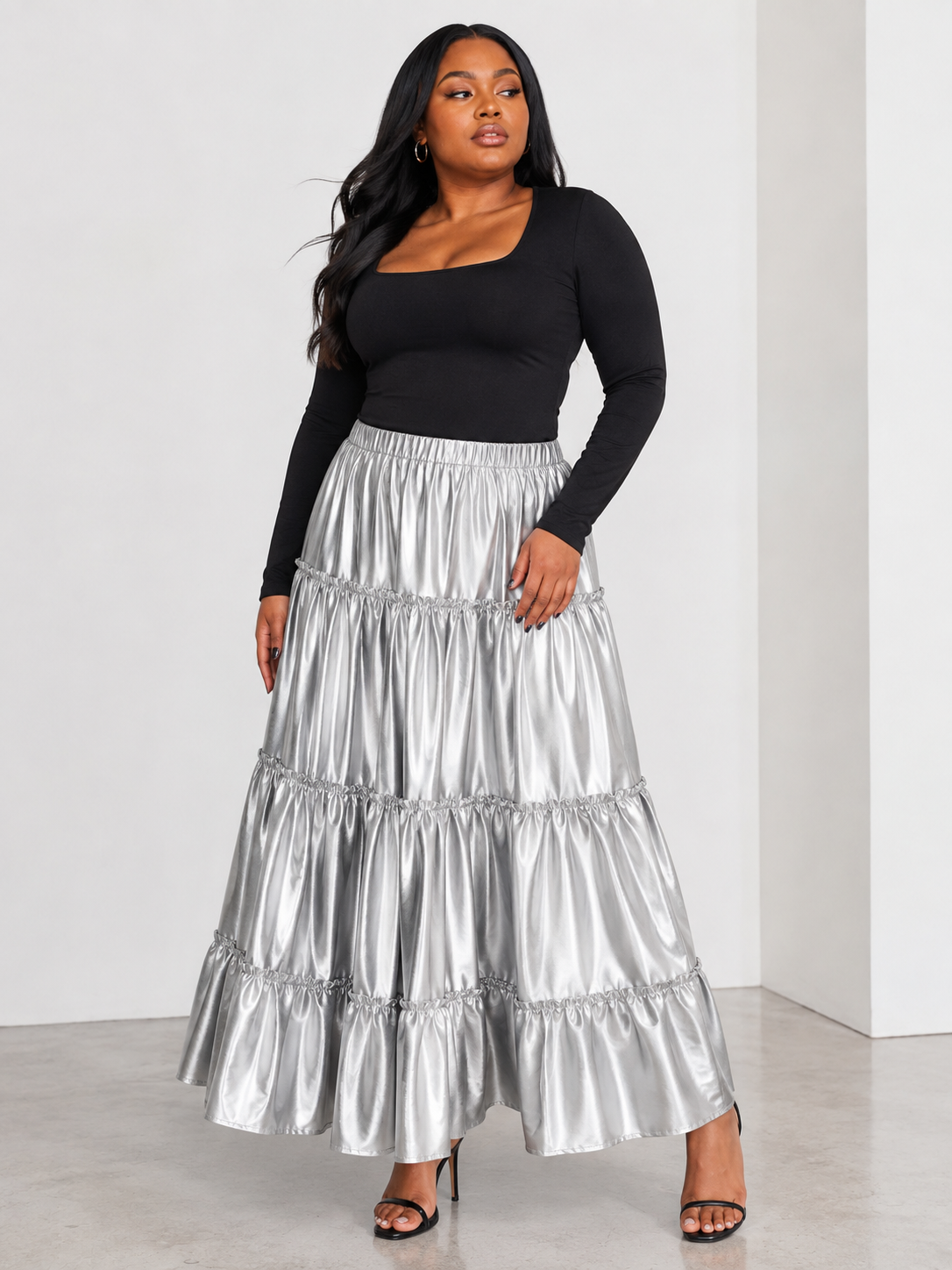 Model wearing the silver metallic tiered maxi skirt standing front facing, showcasing lustrous finish and dramatic tiered silhouette by For Her NYC
