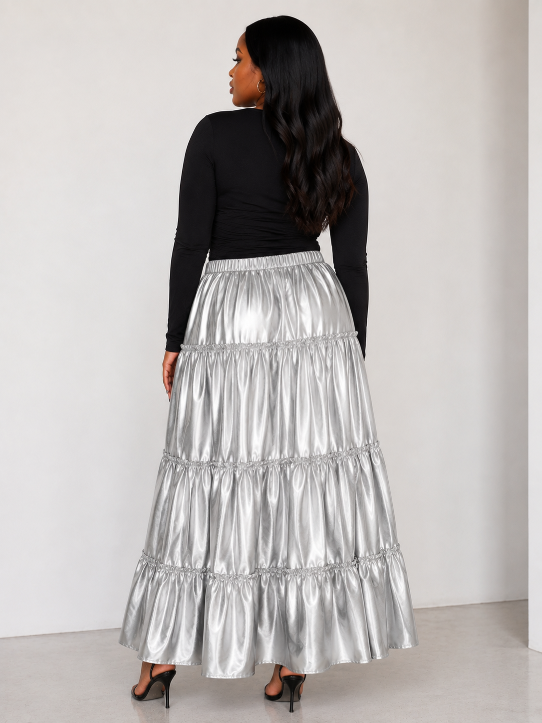 Model wearing the silver metallic tiered maxi skirt standing back facing, showcasing lustrous finish and dramatic tiered silhouette by For Her NYC