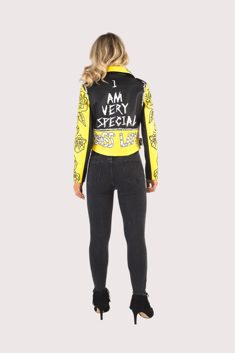 Model wearing multicolor faux leather jacket with pins and studs, full back view highlighting statement text detail and yellow printed sleeves by For Her NYC