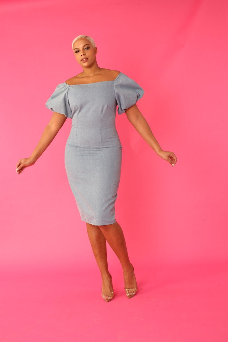 Model walking forward in a blue off-shoulder denim pencil dress with puff sleeves — For Her NYC.