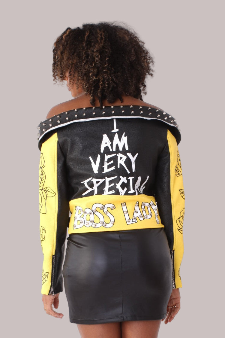 Back: Off-the-shoulder graffiti faux leather jacket in black and yellow, back view, For Her NYC.