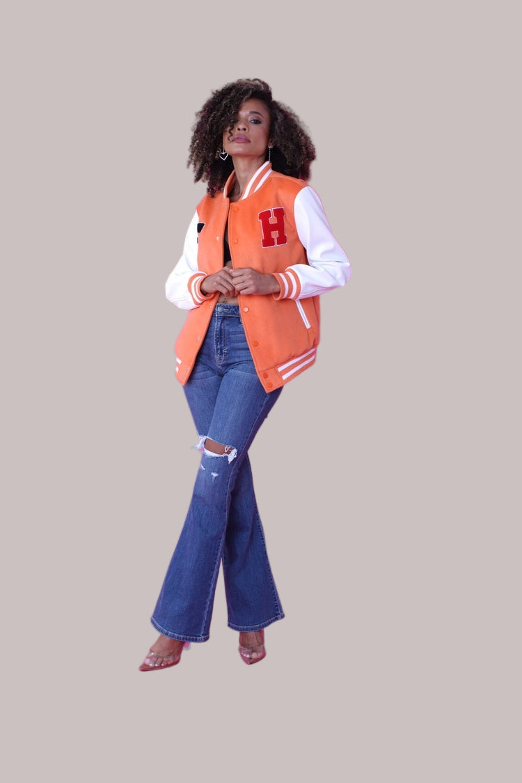 alt text: Side view pose of orange varsity jacket with white sleeves and patches – For Her NYC