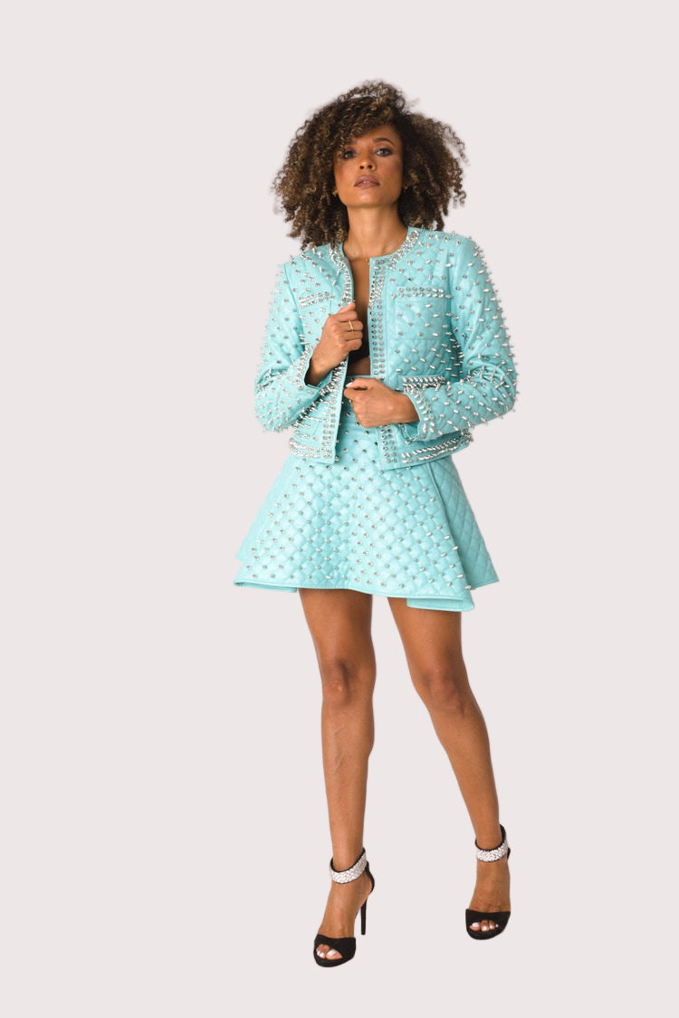 Model wearing pleather quilted flared skirt with studs in turquoise, front-facing hero pose highlighting flared silhouette, quilted texture, and statement stud detailing by For Her NYC