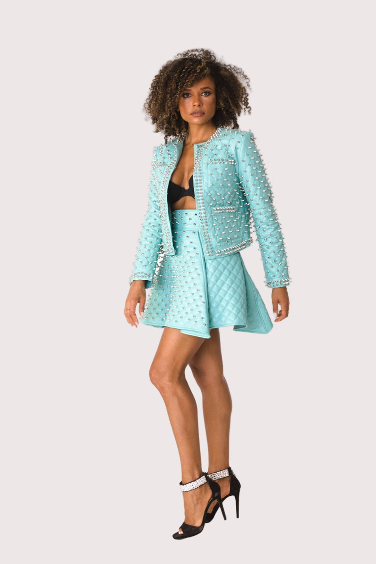 Model wearing pleather quilted flared skirt with studs in turquoise, front walking pose showcasing movement, structured flare, and edgy stud accents by For Her NYC